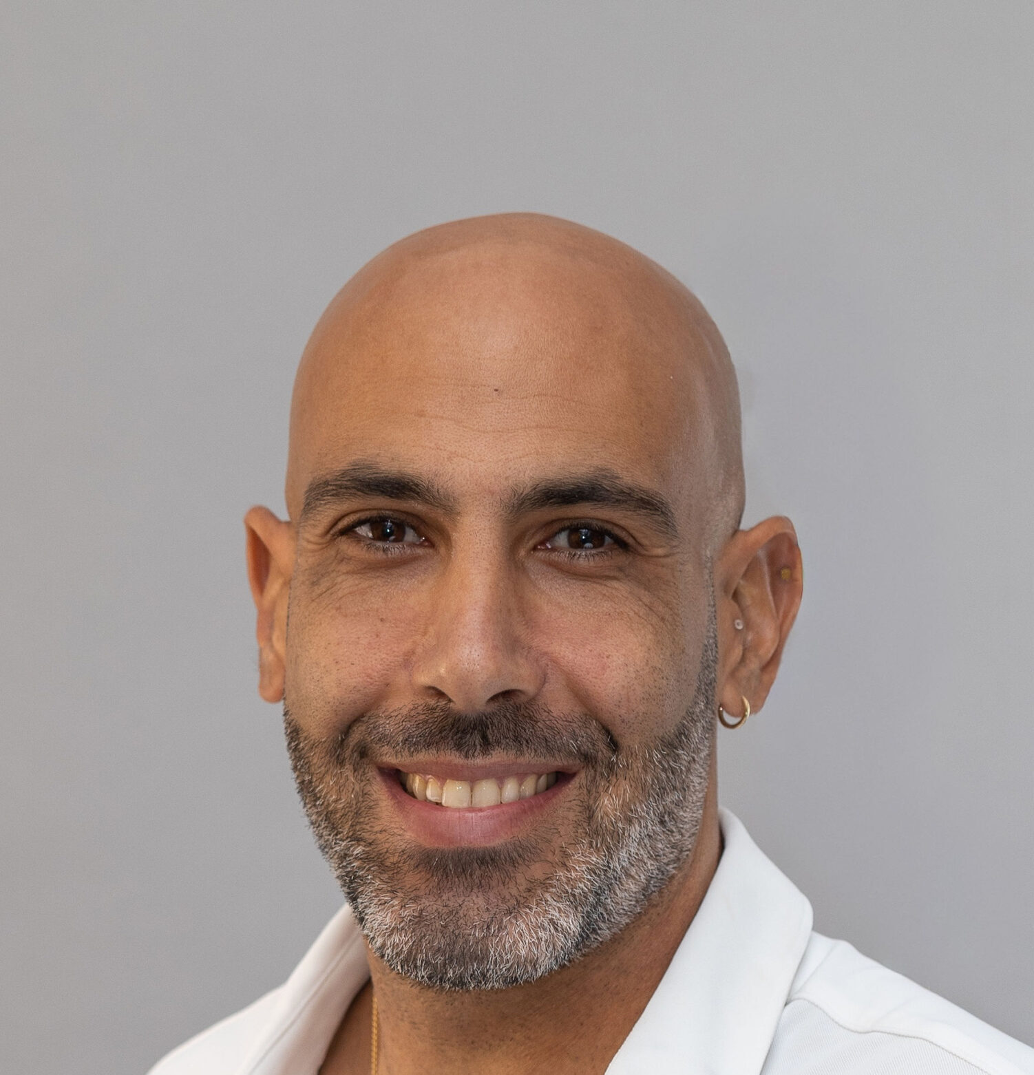 גבר קירח עם זקן קצר מחייך למצלמה על רקע אפור